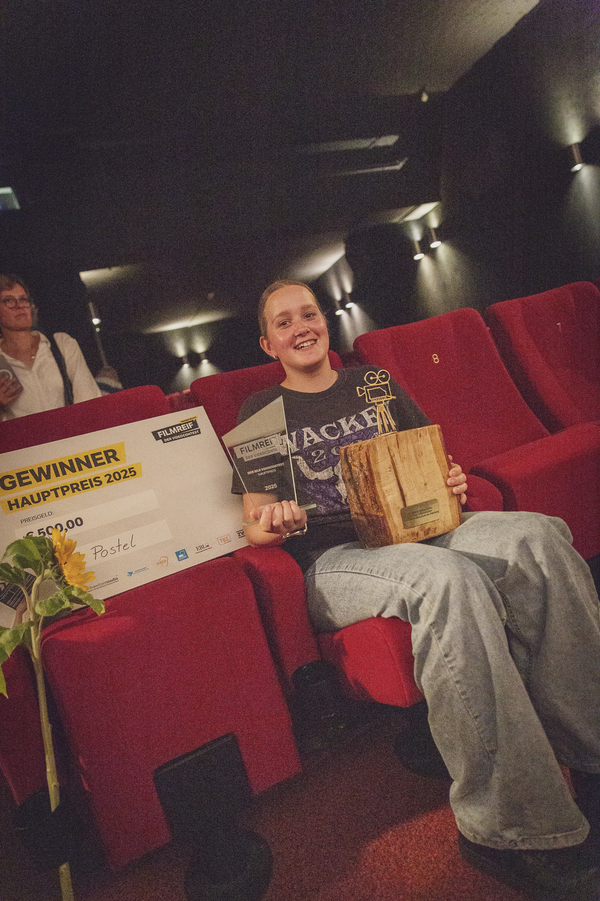 eine Schülerin zeigt den Gewinnerscheck und den Pokl. 