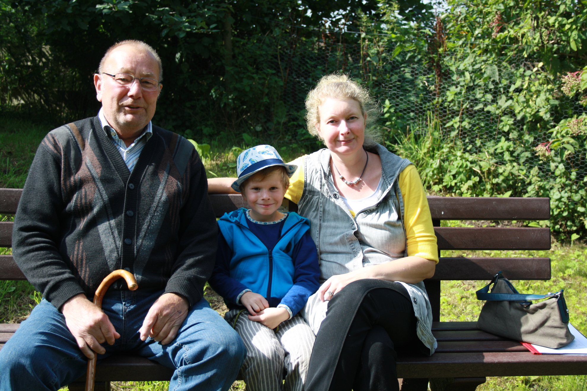 Großvater, Enkel und Mutter sitzen auf einer Bank im Garten.