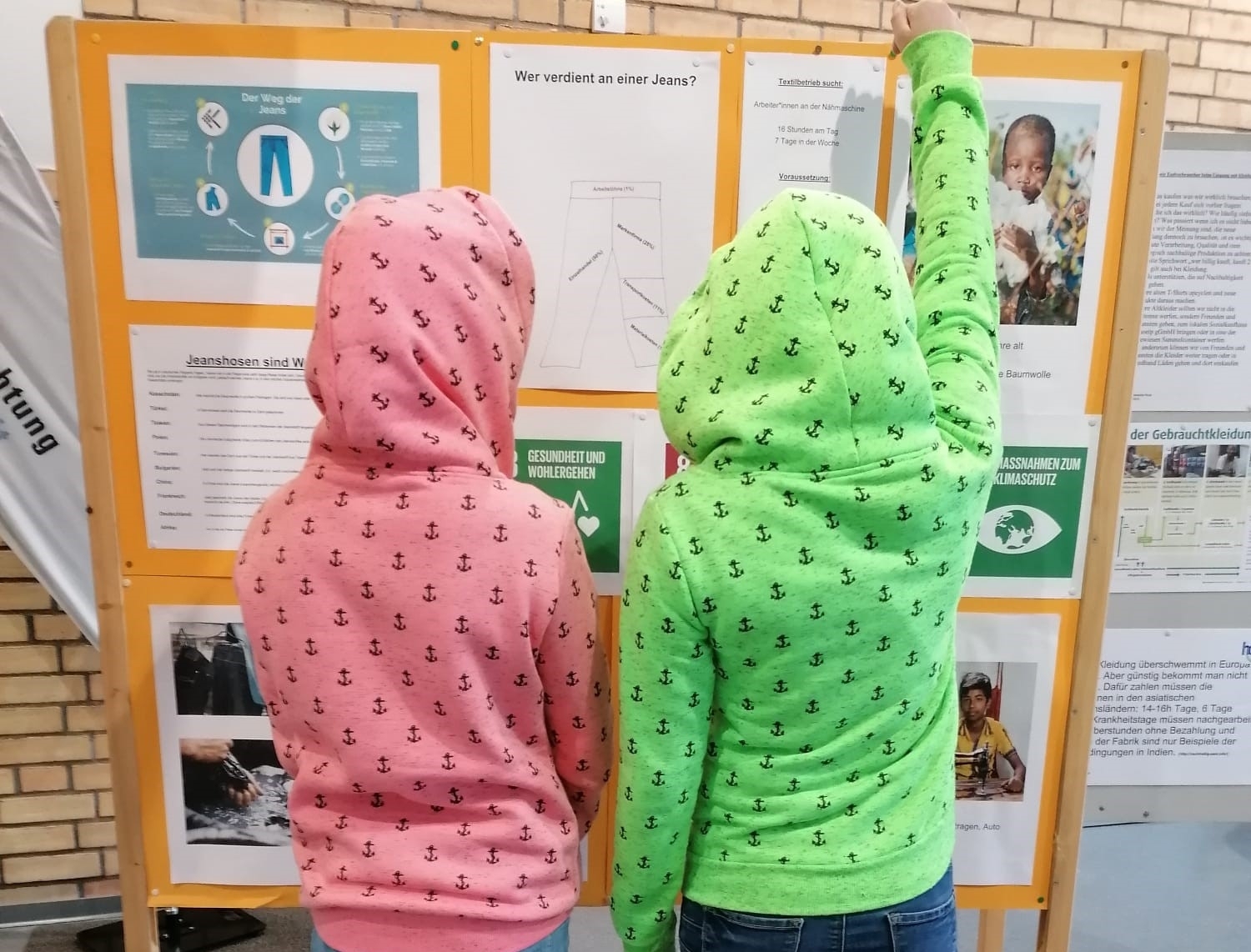 Kinder betrachten Pinnwand - sie tragen bunte Jacken und wirken sehr interessiert.