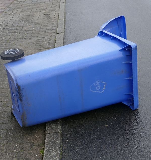 Blaue Papiertonne liegt umgeweht auf der Straße.